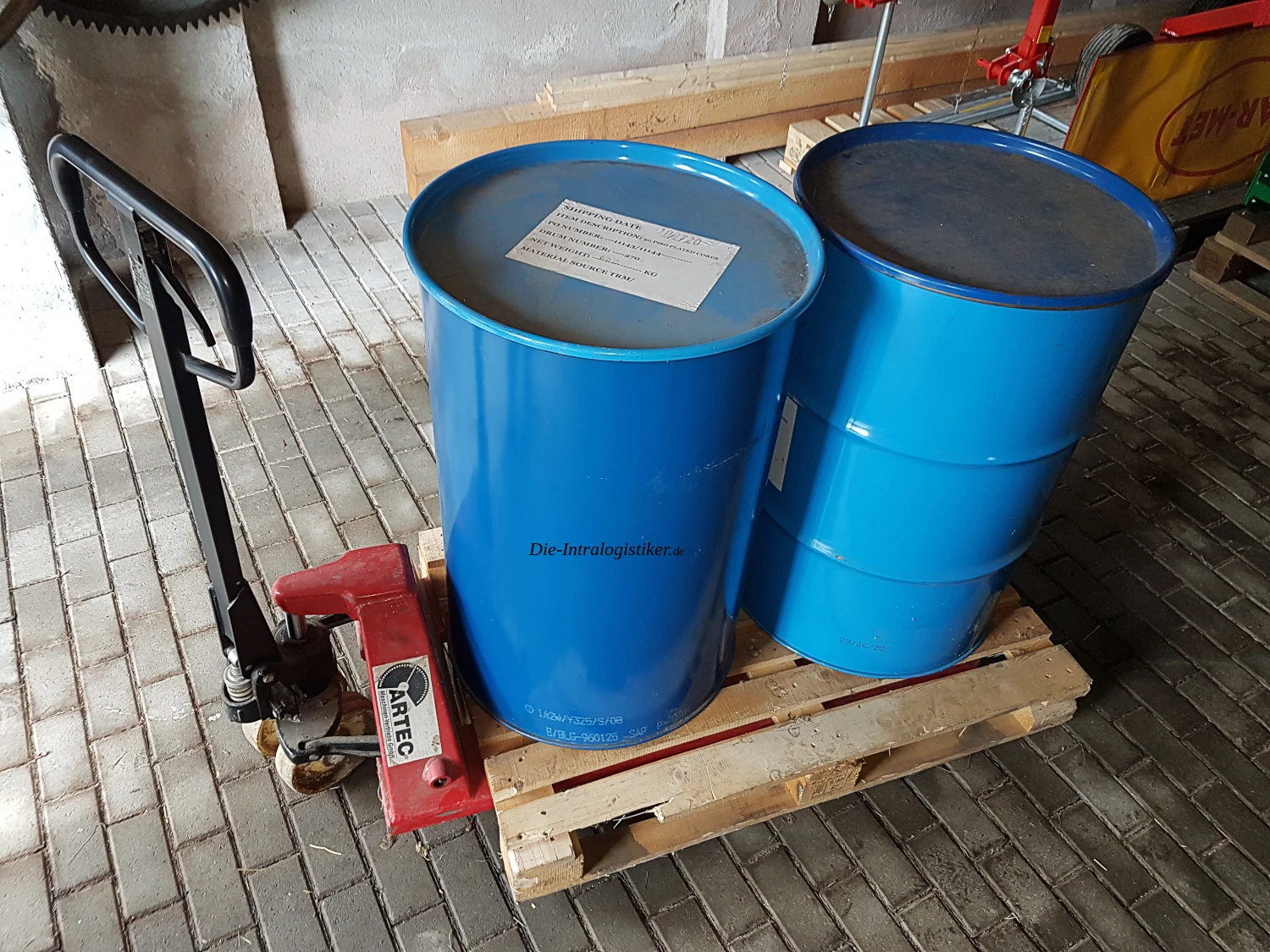 Niederhubwagen transportiert eine Palette mit Industriefässern im Lager